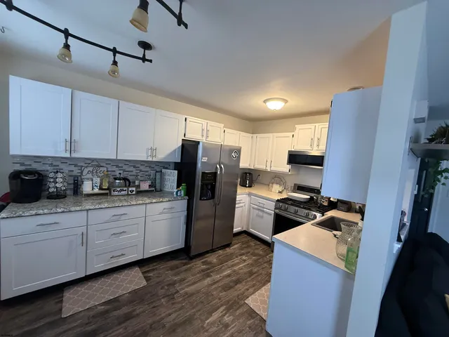 a kitchen with a refrigerator stove and white cabinets with wooden floor