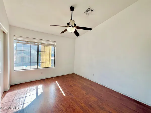 an empty room with wooden floor ceiling fan and windows