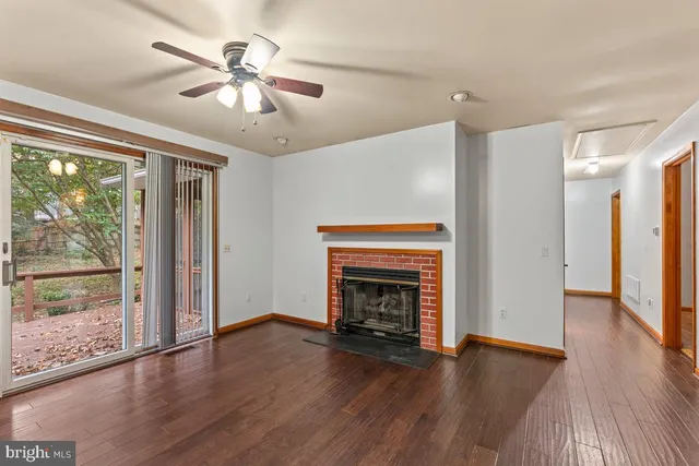 a view of an empty room with wooden floor fireplace and a window