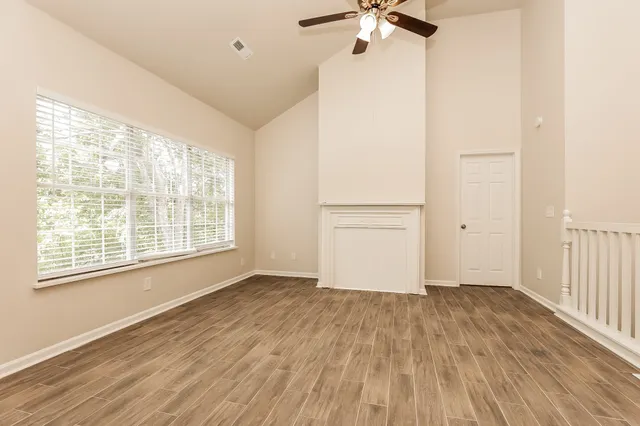 an empty room with wooden floor chandelier fan and windows