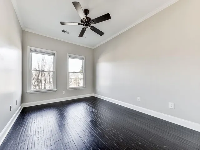 an empty room with wooden floor fan and windows