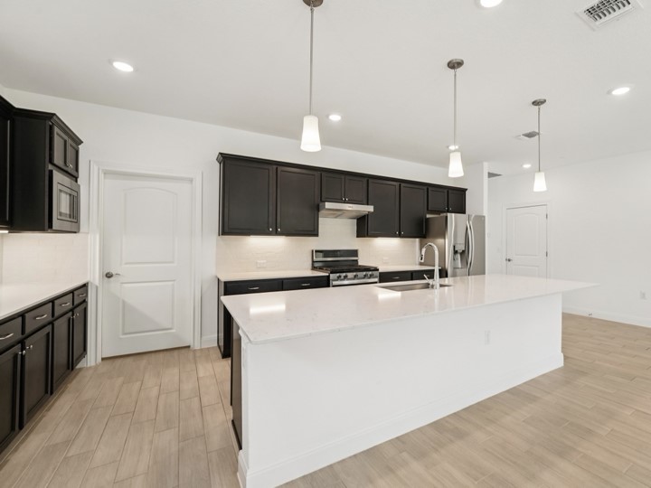 312 Kitty Hawk Road Georgetown, TX 78633 - Photo 11 of 37 a large white kitchen with kitchen island a sink a stove and a wooden floors