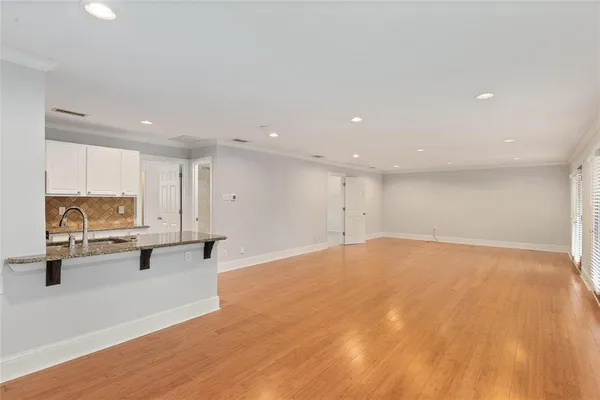 a view of an empty room with kitchen view and wooden floor