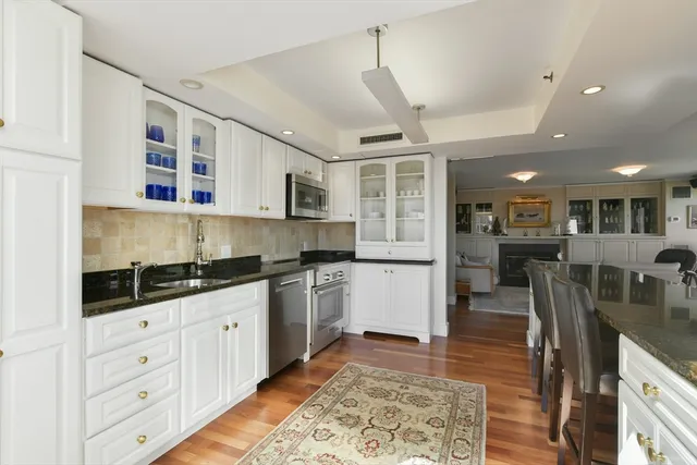 a kitchen with stainless steel appliances kitchen island granite countertop a refrigerator a stove a sink a oven with white cabinets and wooden floor