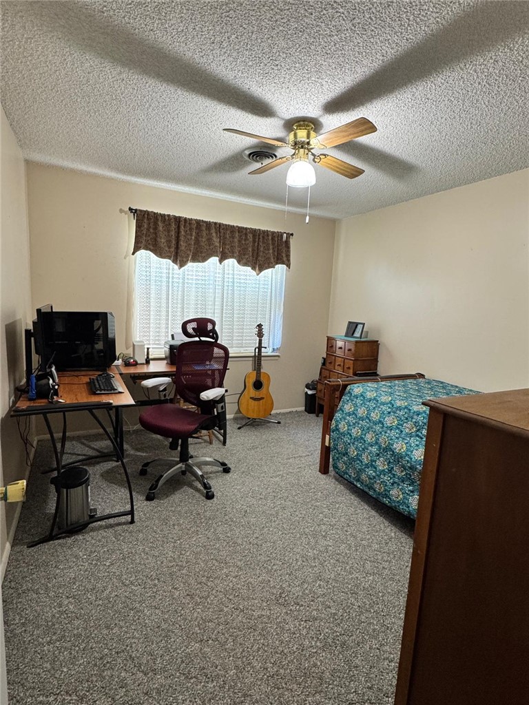 Carpeted bedroom featuring an office area, a textured ceiling, and a ceiling fan