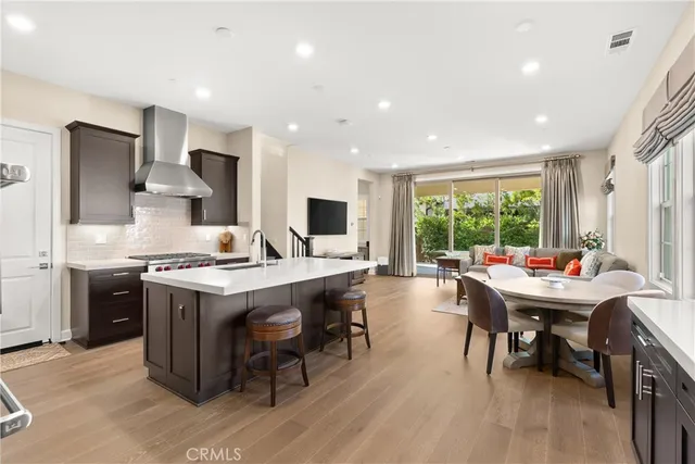 a kitchen with stainless steel appliances granite countertop a stove top oven a sink dishwasher a dining table and chairs with wooden floor