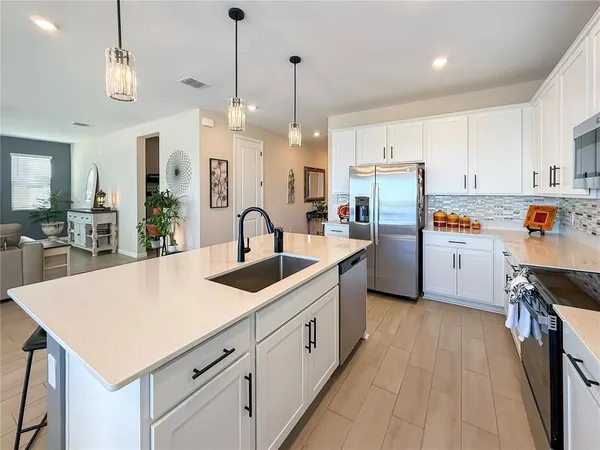a open kitchen with stainless steel appliances granite countertop a refrigerator a stove top oven a sink dishwasher and white cabinets with wooden floor
