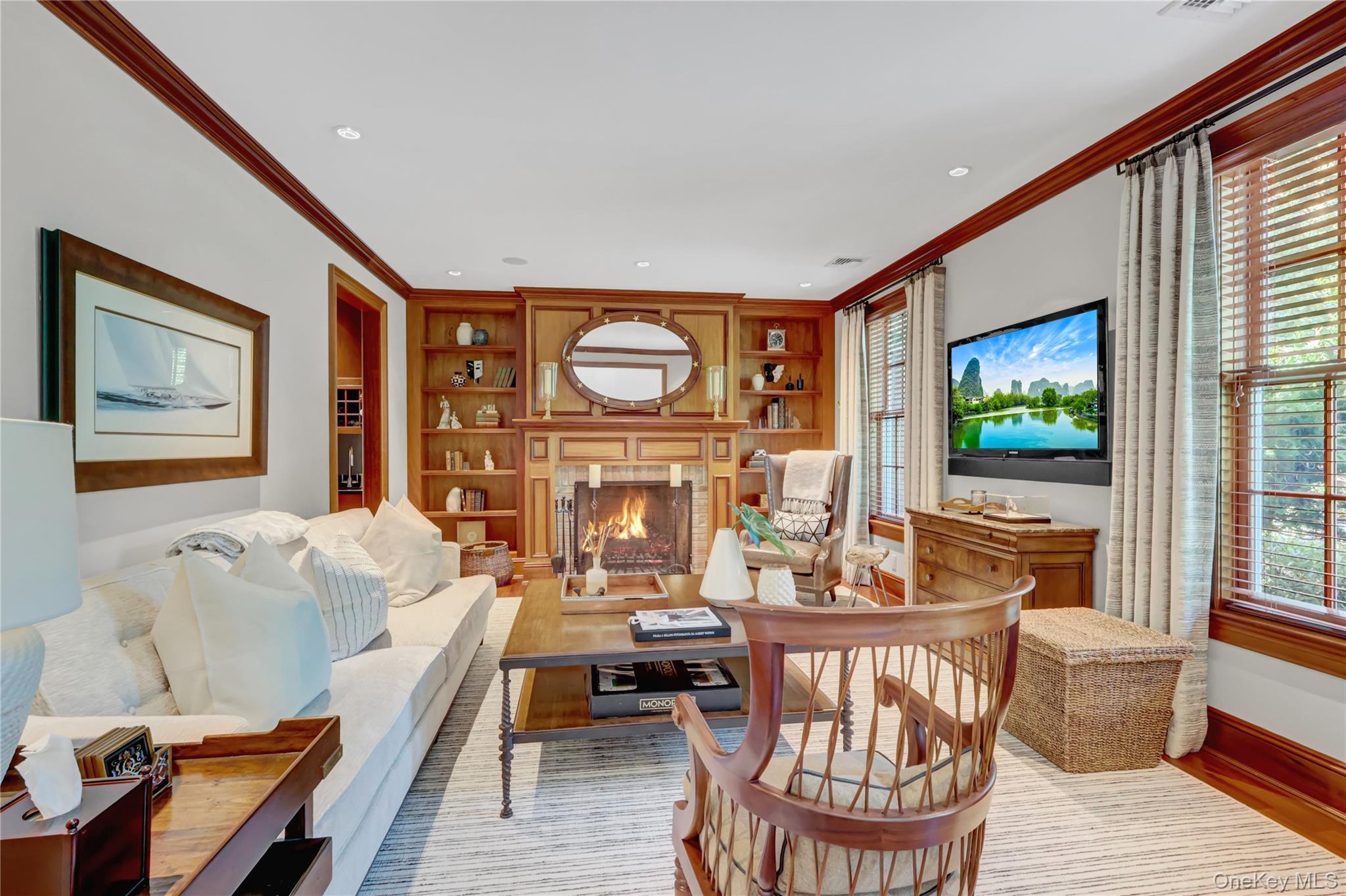 63 Dyke Road Setauket, NY 11733 - Photo 7 of 49 Living room featuring built in shelves, crown molding, light wood finished floors, plenty of natural light, and a lit fireplace