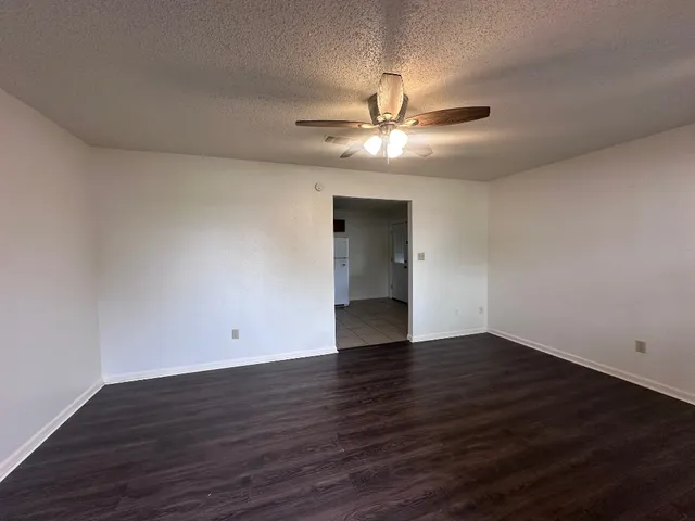 a view of an empty room with wooden floor and a ceiling fan
