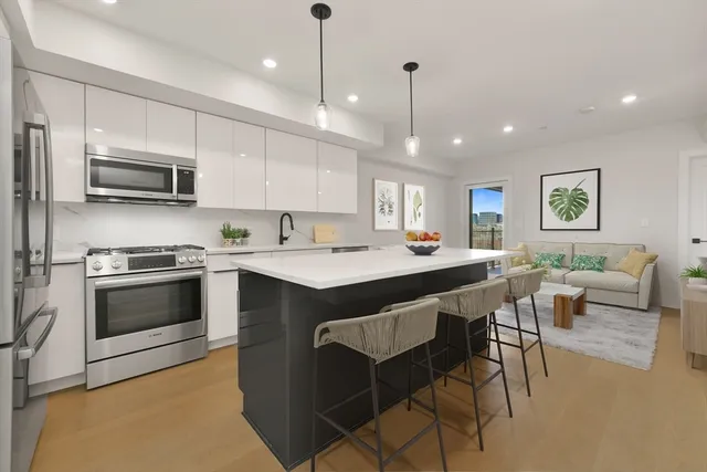 a kitchen with stainless steel appliances granite countertop a stove a sink a microwave a refrigerator and white cabinets with wooden floors