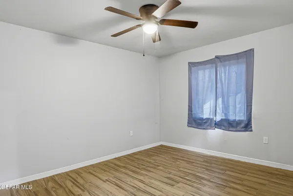 an empty room with wooden floor chandelier fan and windows