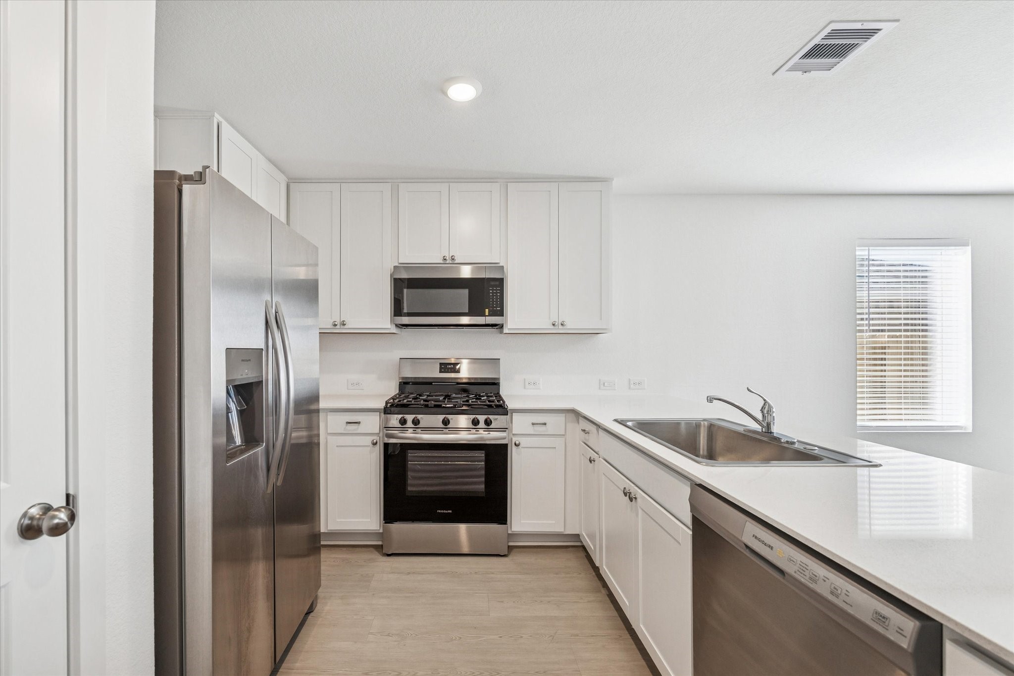 16207 Rustic Prairie Drive Hockley, TX 77447 - Photo 3 of 11 Crisp and modern, the kitchen features white shaker cabinetry, sleek quartz countertops, and a large stainless steel sink beneath a picture window, bringing in natural light while overlooking the backyard.