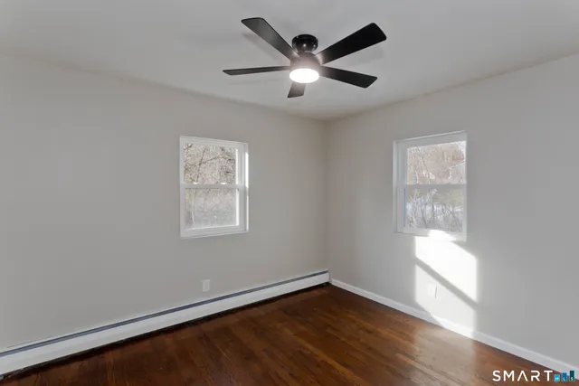 an empty room with wooden floor fan and windows