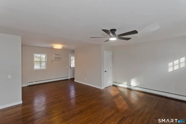 a view of an empty room with wooden floor and a ceiling fan
