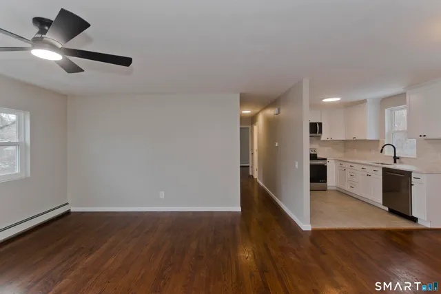 a view of an empty room with wooden floor and a ceiling fan