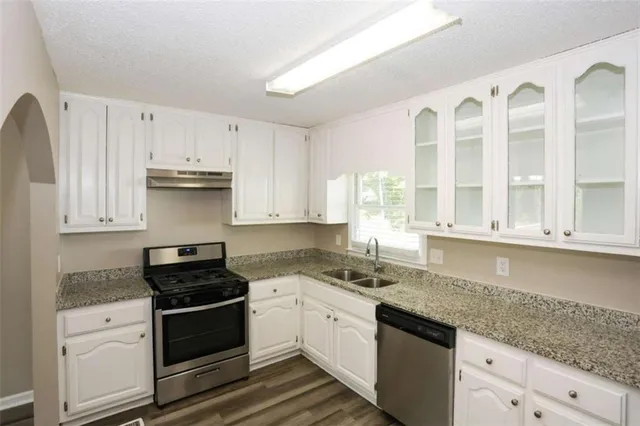 a kitchen with granite countertop a sink cabinets stainless steel appliances and a window