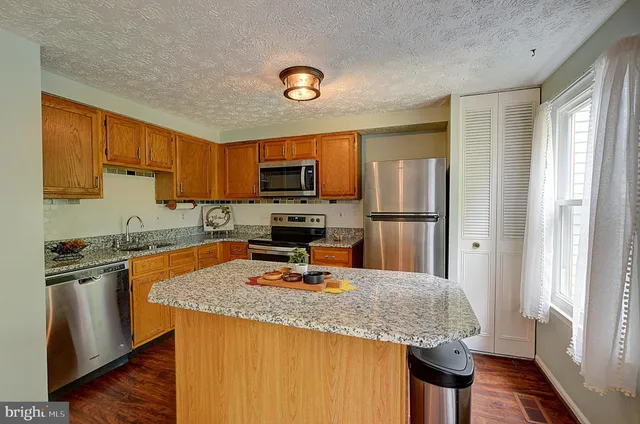 a kitchen with granite countertop stainless steel appliances a sink refrigerator stove and microwave