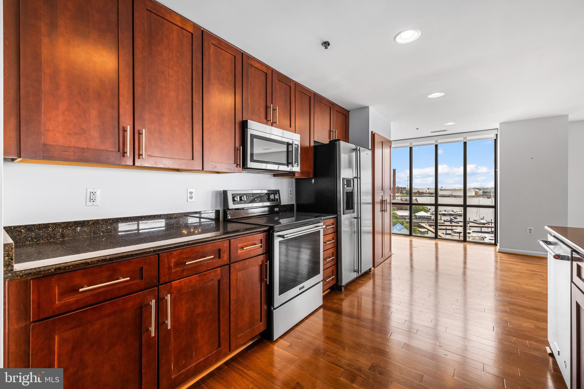 2702 Lighthouse Point East, Unit 638 Baltimore, MD 21224 - Photo 15 of 72 a kitchen with stainless steel appliances granite countertop wooden cabinets a stove top oven a sink and dishwasher with wooden floor