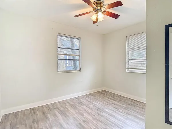 an empty room with wooden floor chandelier fan and windows