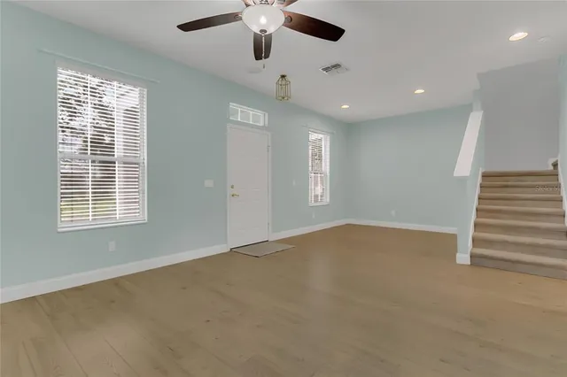 an empty room with wooden floor ceiling fan and windows