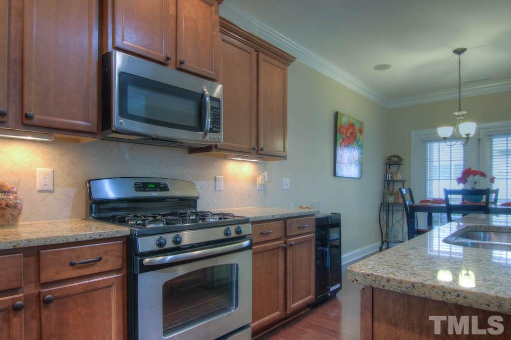 605 Democracy Street Raleigh, NC 27603 - Photo 6 of 25 a kitchen with stainless steel appliances granite countertop a stove a microwave and wooden cabinets