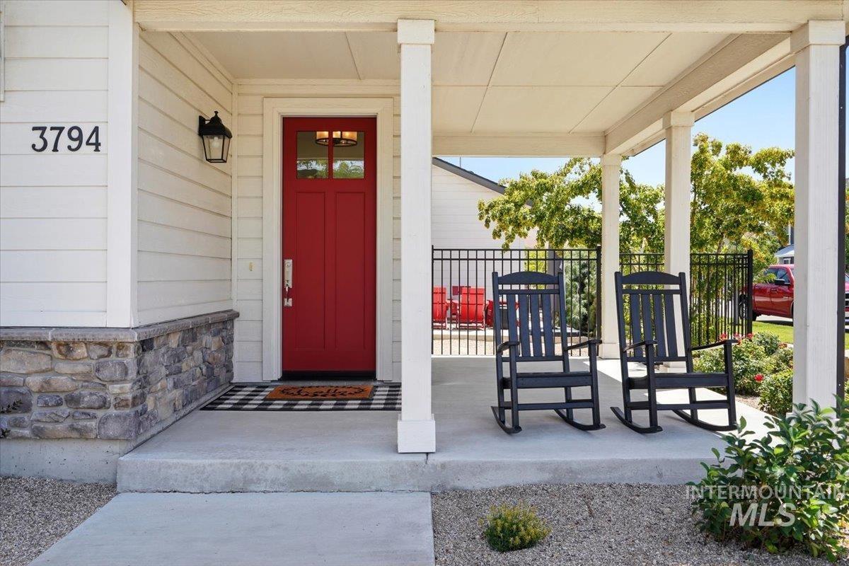 3794 South Single Tree Avenue Boise, ID 83716 - Photo 6 of 50 Covered porch featuring a red entry door with transom window, stone veneer siding, and a black wrought iron fence