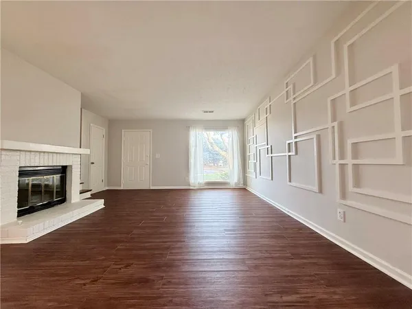 a view of an empty room with wooden floor fireplace and a window