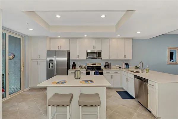 a kitchen with stainless steel appliances kitchen island granite countertop a sink a stove a refrigerator with white cabinets and wooden floor