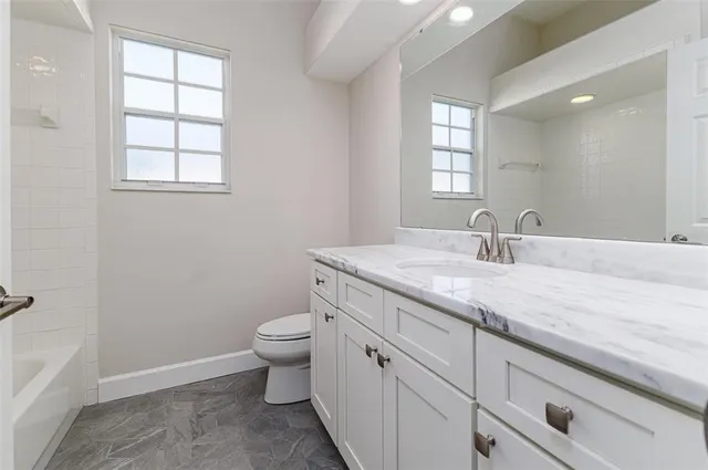 a bathroom with a granite countertop sink a toilet and a window