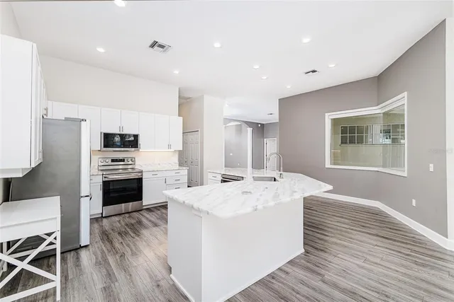 a large kitchen with kitchen island a stove a sink a refrigerator and white cabinets with wooden floor