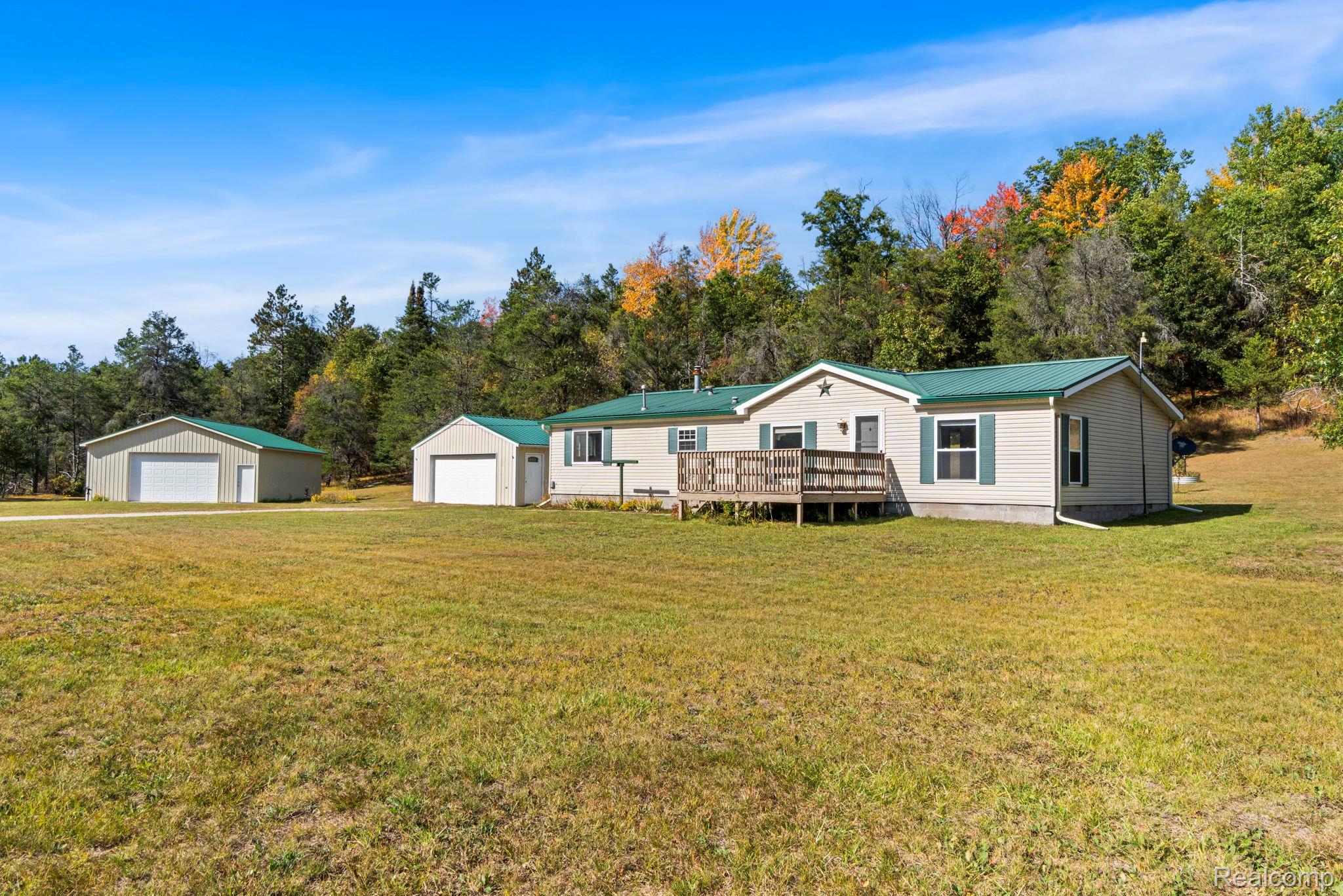 Siding exterior with a green metal roof, a wooden deck, and an attached single-car garage