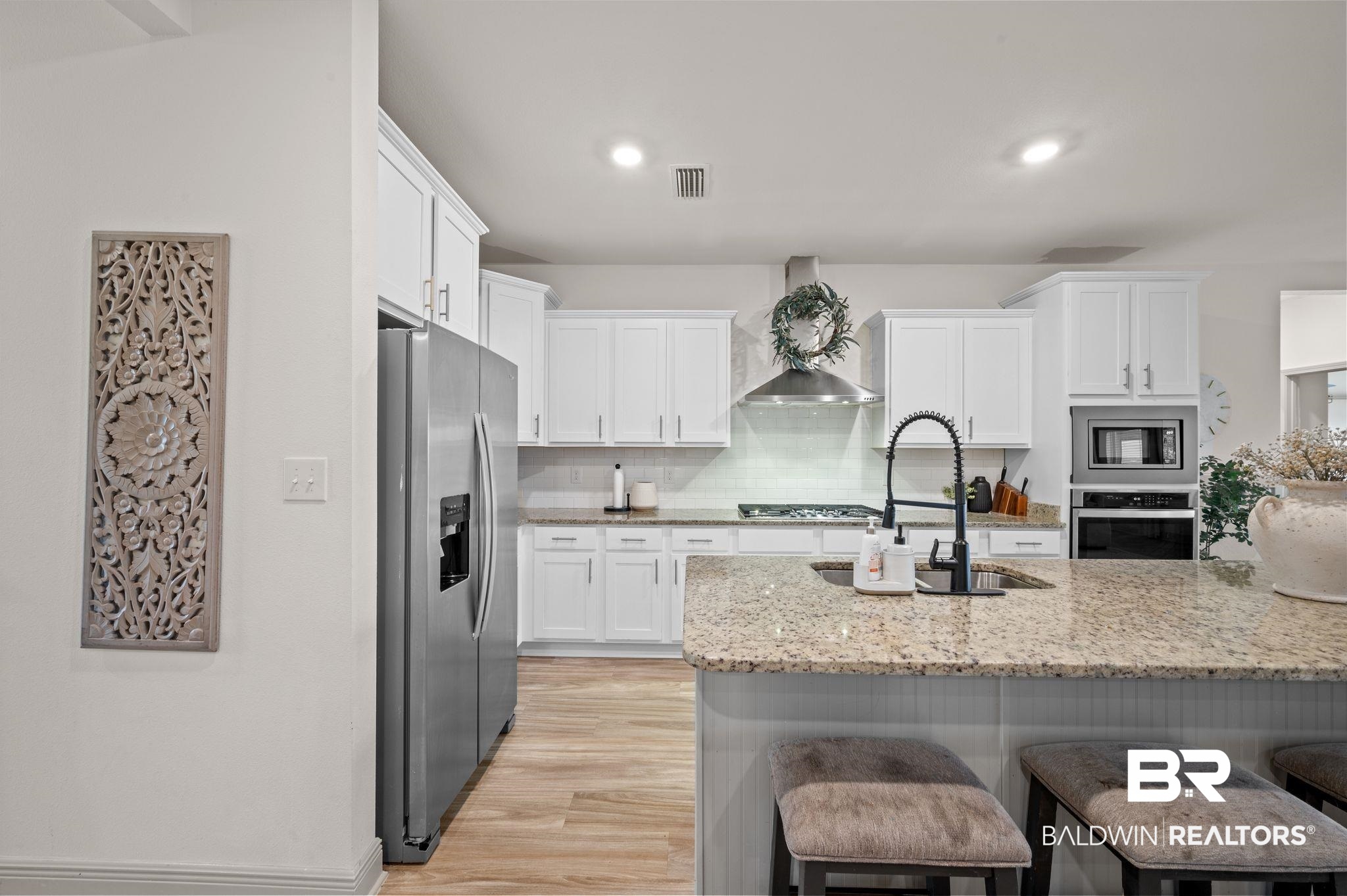 10169 Dunleith Loop Daphne, AL 36526 - Photo 27 of 40 Kitchen featuring appliances with stainless steel finishes, white cabinetry, a kitchen bar, wall chimney exhaust hood, and light wood-style flooring