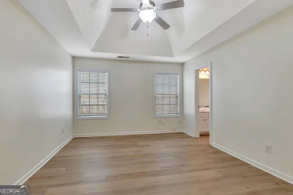 an empty room with wooden floor chandelier fan and windows