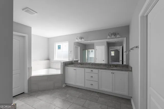 a spacious bathroom with a granite countertop sink a mirror and a bathtub