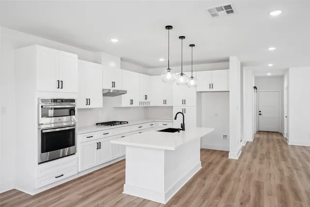 a kitchen with stainless steel appliances kitchen island granite countertop a sink a stove a refrigerator and white cabinets with wooden floor