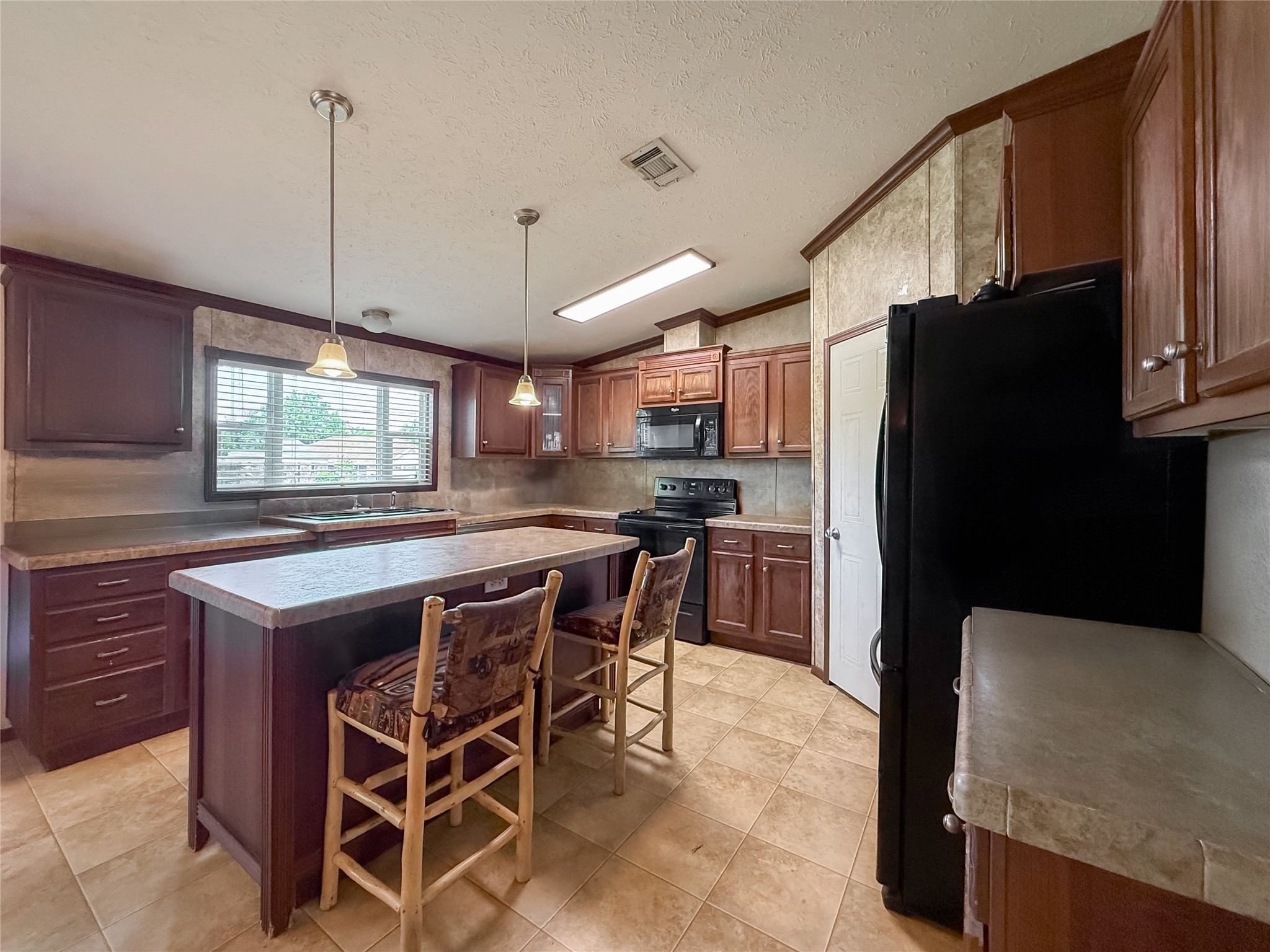 845 Caldwell Street Lexington, TX 78947 - Photo 3 of 39 Kitchen featuring black appliances, a kitchen island, a kitchen breakfast bar, light tile patterned floors, and ornamental molding