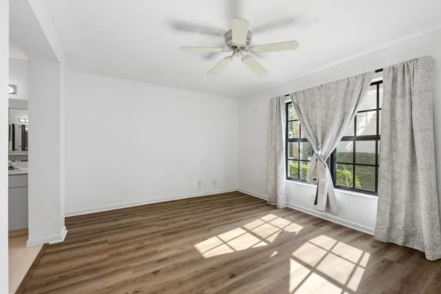 an empty room with wooden floor fan and windows