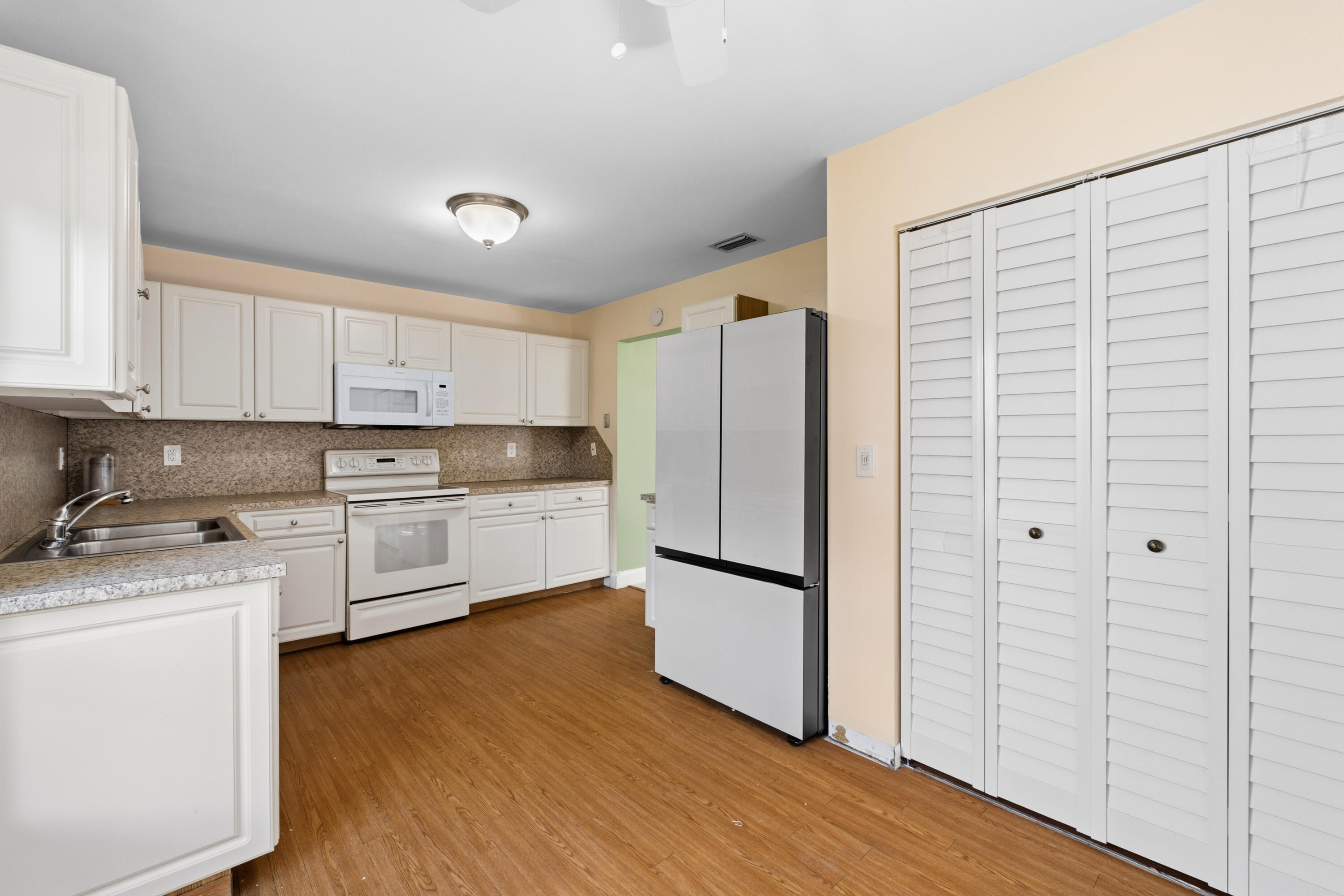 3233 Perimeter Drive, Unit 2511 Greenacres, FL 33467 - Photo 4 of 39 a kitchen with stainless steel appliances granite countertop a refrigerator a stove and white cabinets with wooden floor