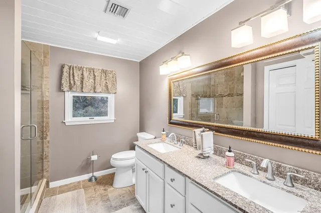 a bathroom with a granite countertop sink a large mirror a toilet and a window