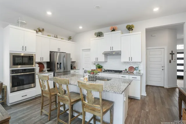 a kitchen with stainless steel appliances a dining table chairs microwave and refrigerator