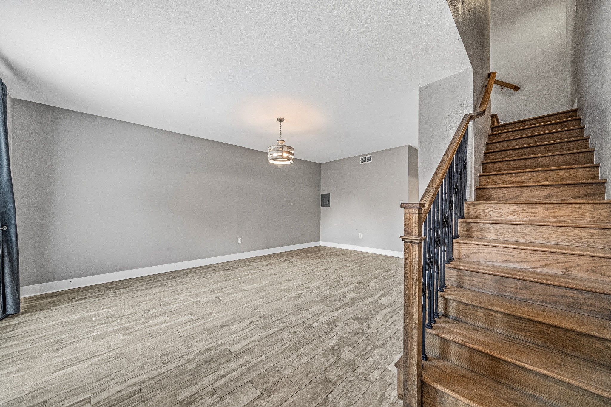 830 Threadneedle Street, Unit 240 Houston, TX 77079 - Photo 5 of 33 This photo shows a bright, open living area with light wood flooring and neutral gray walls. A modern light fixture hangs from the ceiling. To the right, there is a staircase with wooden steps and wrought iron railing, adding a touch of elegance to the space.