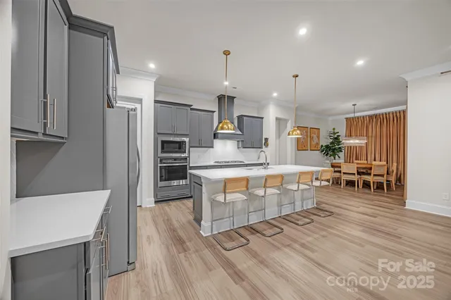 a kitchen with stainless steel appliances a stove top oven a sink dishwasher and a refrigerator with wooden floor