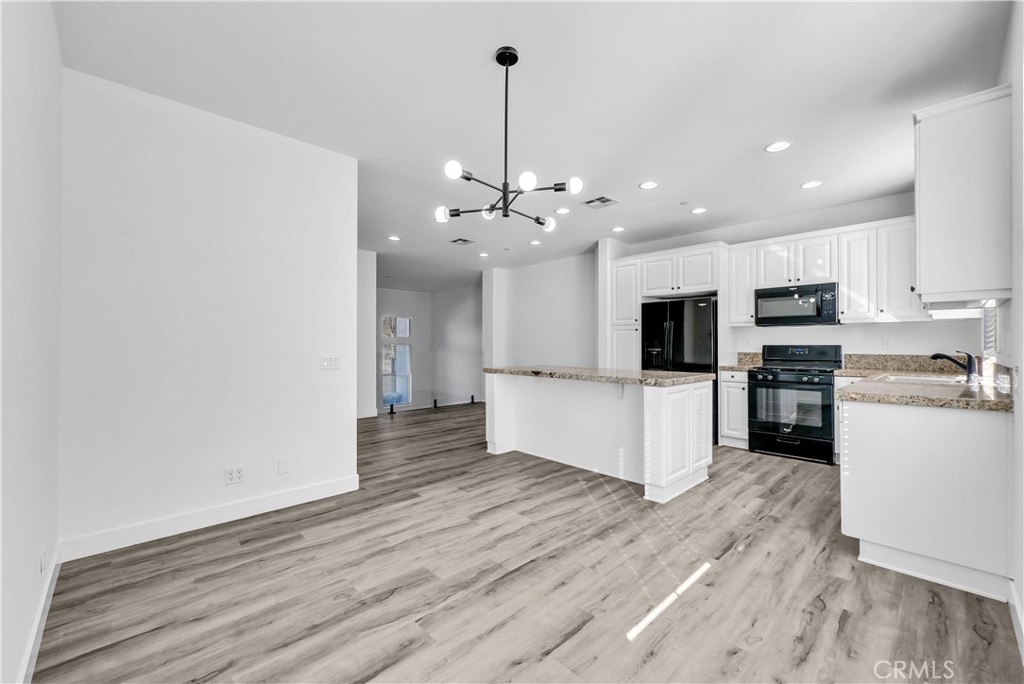 8415 Kendra Loop Orange, CA 92867 - Photo 17 of 36 a large kitchen with kitchen island a stove a sink a refrigerator and white cabinets with wooden floor