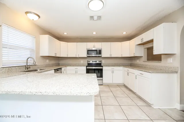 a large kitchen with granite countertop a sink white cabinets and a stove