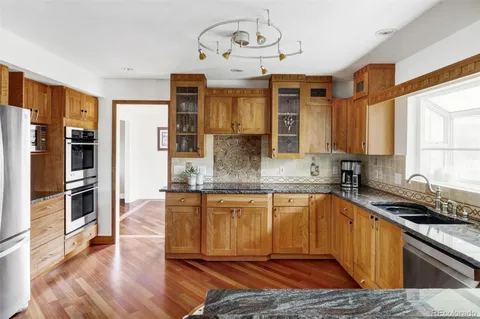 a kitchen with stainless steel appliances granite countertop a refrigerator a sink dishwasher a stove and white countertops with wooden floor