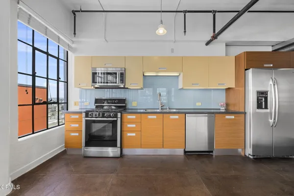 a kitchen with stainless steel appliances granite countertop a refrigerator a sink dishwasher a stove and a dining table with wooden floor