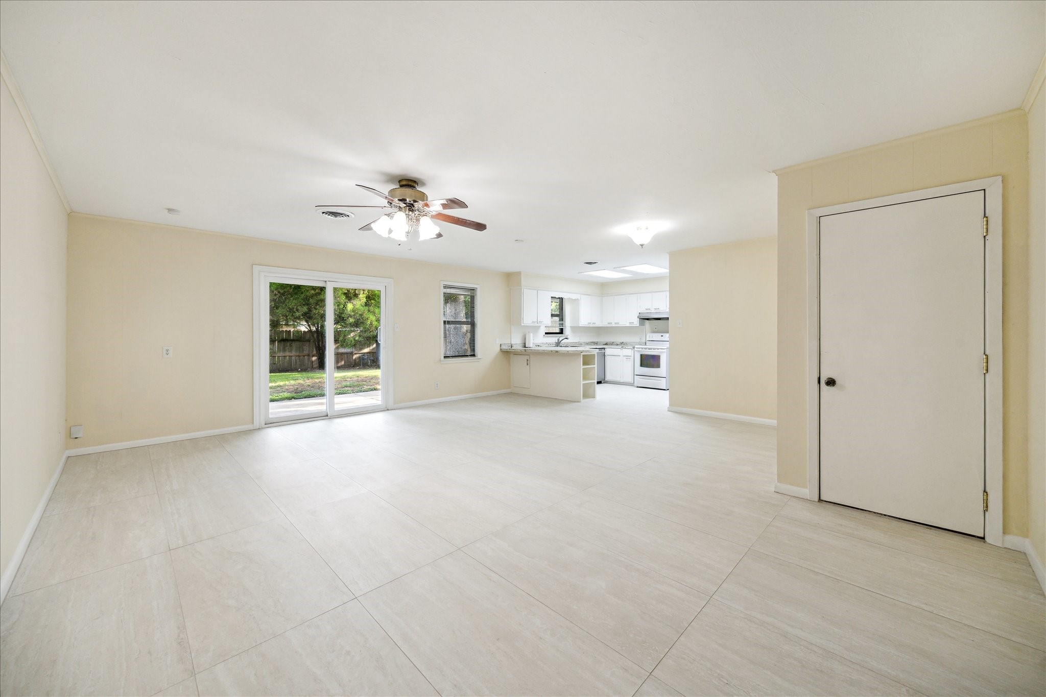 8907 Autauga Street Houston, TX 77080 - Photo 6 of 20 This spacious, open-concept living area features neutral-toned tile flooring, a ceiling fan, and ample natural light from large sliding glass doors. It seamlessly connects to a modern kitchen with white cabinetry, offering a bright and inviting atmosphere.