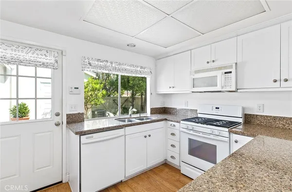 a kitchen with granite countertop a stove a sink and white cabinets