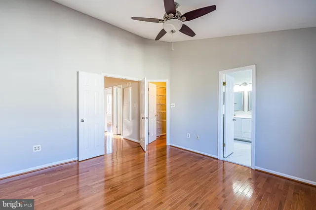 an empty room with wooden floor a ceiling fan and windows