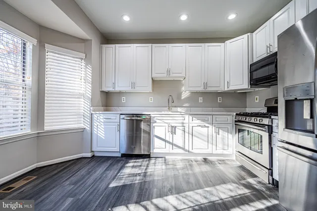 a kitchen with granite countertop a stove top oven a sink dishwasher and white cabinets with wooden floor